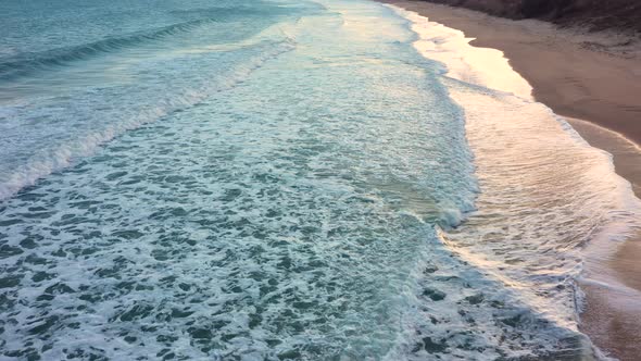 Aerial view of waves crash to shore at sunset