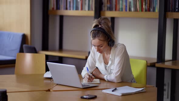 Blonde Woman Study at Distant Learning at Library Taking Notes