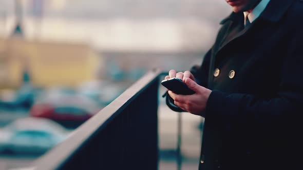 Businessman in a black coat standing on the street surfing in a smartphone on the phone