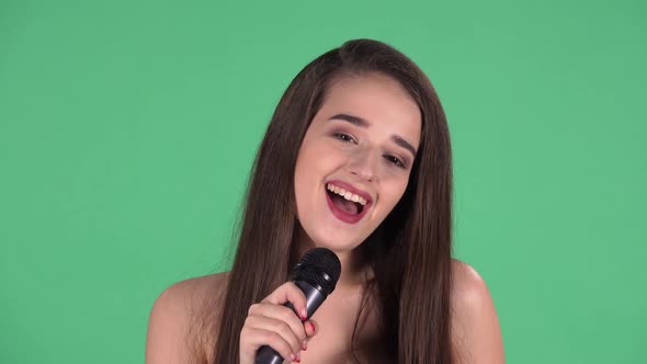 Portrait of Beautiful Young Woman Coquettishly Looking at Camera and Sings Song Into Microphone