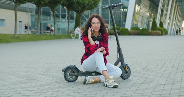 Woman with Earphones which Sitting on E-scooter and Enjoing Her Mobile