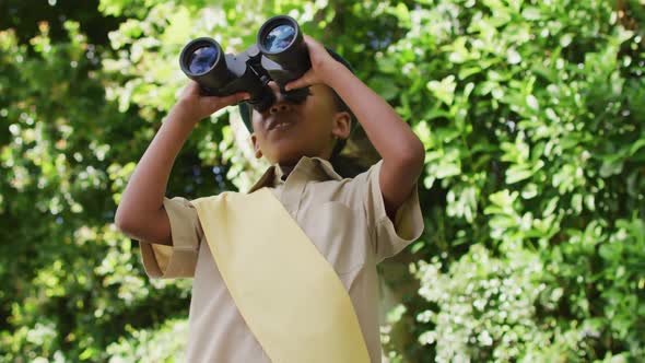 Animation of african american girl in scout costume using binoculars in garden