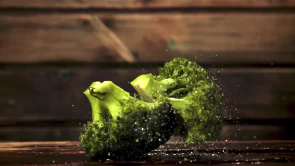 Super Slow Motion Pieces of Broccoli Fall on the Table with Splashes of Water