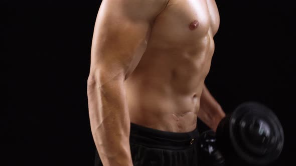 Man Flexes His Hands with Dumbbells Training His Biceps on a Black Background in the Studio