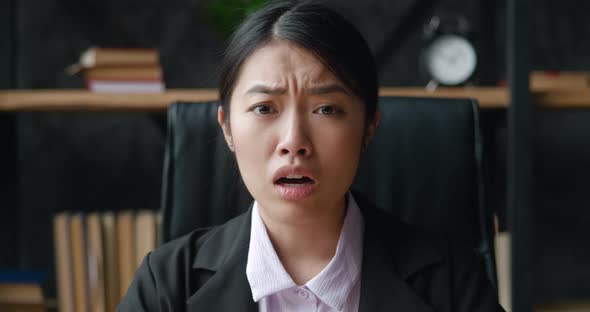 Shocked Asian Business Woman Looks at the Camera with Fear of Terrible News While Sitting at Office