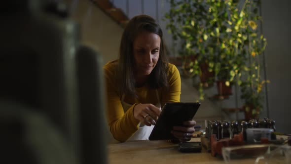 Caucasian female jeweller in workshop wearing apron, using tablet, smiling at camera