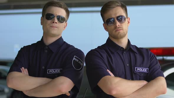 Confident Policemen in Sunglasses Crossing Hands on Chest Standing Near Cop Car