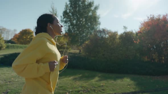 Girl Running on Path at the City Park on a Sunny Autumn Day Using Headphones