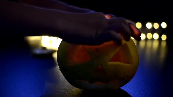 A Man Lights a Candle in an Orange Halloween Pumpkin on a Dark Background with a Bokeh Photo