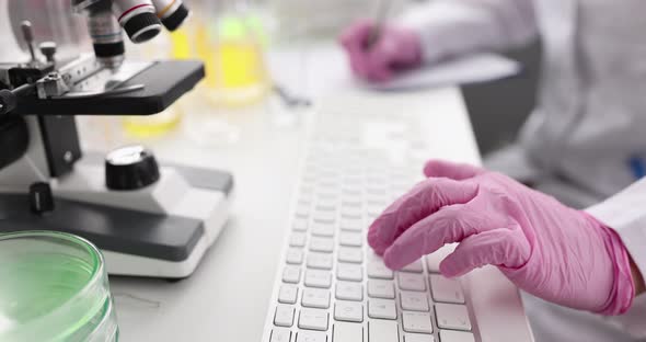 Doctor Scientist with Gloves Typing on Keyboard and Writing Down Receiving Data