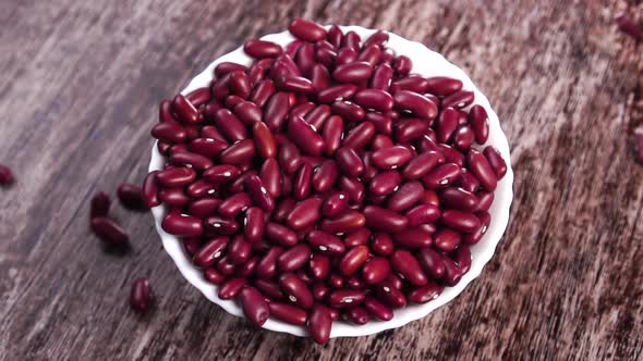 A full white bowl of uncooked red kidney beans on a rustic brown wooden surface