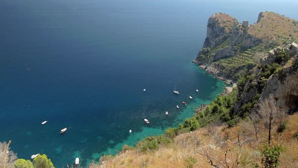 Rocky Coastline And Turquoise Sea Surface With Boats Moored In Amalfi Coast. High Angle, Locked Off