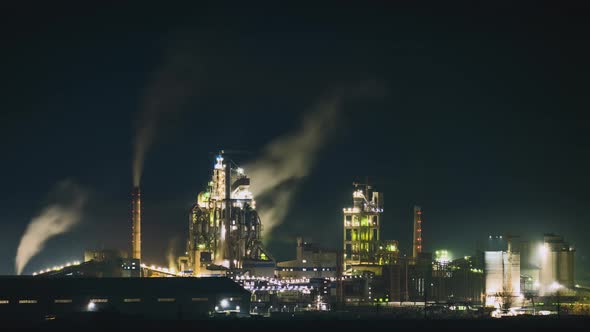 High Concrete Structure of Cement Factory with Tower Crane and Smoking Chimney at Night