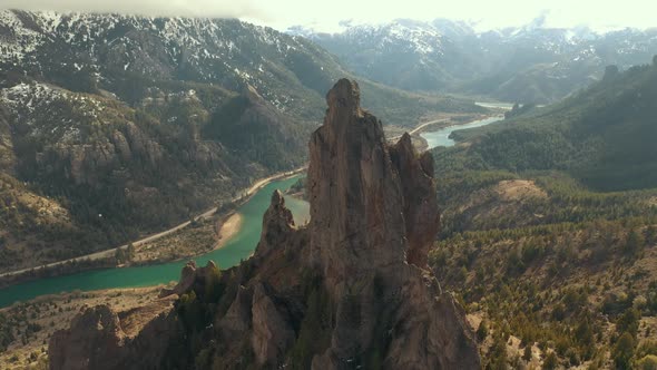 Aerial shot orbiting an impressive rock formation with a river valley on background in Patagonia reg