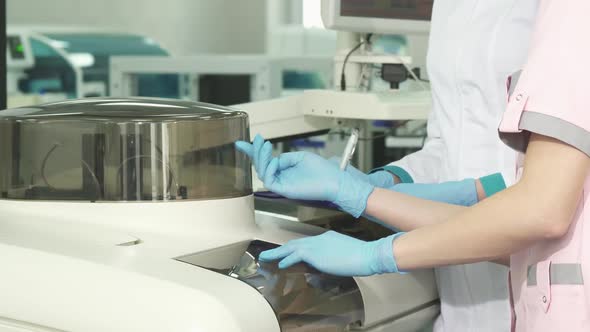 Cropped Shot of Tow Female Laboratory Technicians Examining Analysing Machine