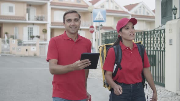 Two Happy Couriers in Red Uniforms Walking Outside