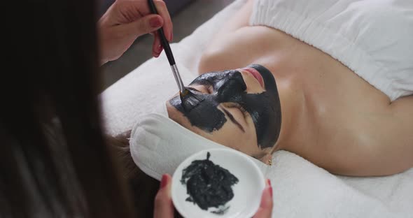 Caucasian woman lying back while beautician gives her a face mask