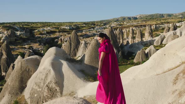 Girl in a Long Purple Dress Stands High on a Rock in Cappadocia