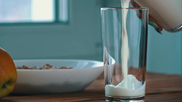 Pouring Milk Into a Glass for Breakfast with Oatmeal in Slow Mo