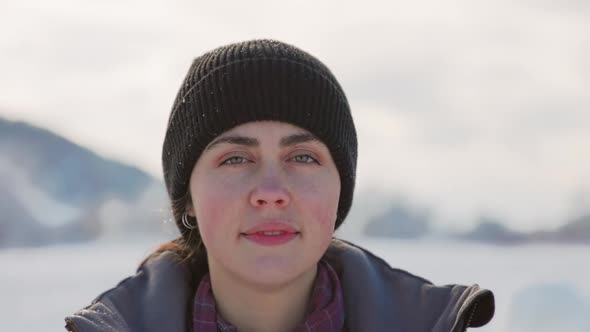 Portrait of a beautiful caucasian smiling young woman in winter clothes and a hat in a snowy park.