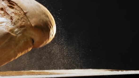Loaf of Homemade Bread with Flour Falls Down Onto Dark Table
