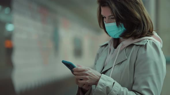 Woman in mask using phone on subway platform