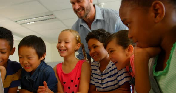 Adult Caucasian male teacher teaching kids on laptop in classroom at school 4k