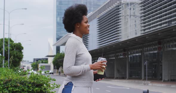 African american businesswoman walking with smartphone and coffee in city