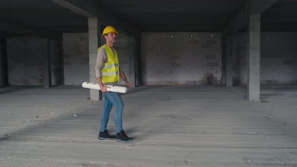 Wide image of caucasian engineer walking on construction site and holding project plans.