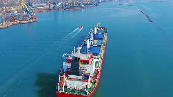 Aerial View. Large Cargo Ship Enters the Port City with Port Cranes.