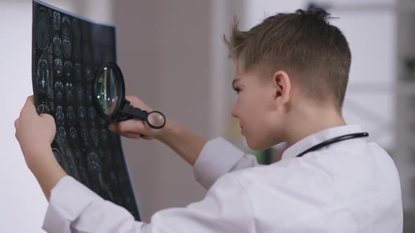 Side View Handsome Focused Teenage Doctor Examining Xray with Magnifying Glass Thinking