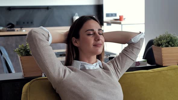 Serene Young Woman Resting on Couch Holding Hands Behind Head Taking Deep Breath of Fresh Air
