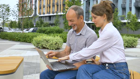 Young Employee is Teaching Her Older Colleague How to Use Laptop and Corporate Software Sitting on