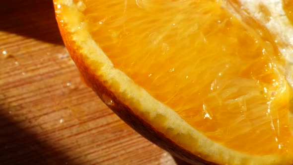 Macro shot on a ripe orange fruit slice with juice dripping off of it in the sunlight on a cutting b