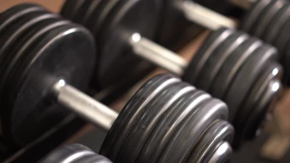 Closeup slow slider shot to the left looking down at severe angle on row of dumbbells on a rack with