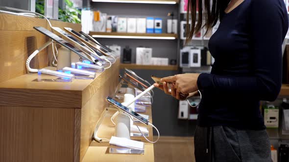 Young Woman Chooses a New Smartphone in an Electronics Store