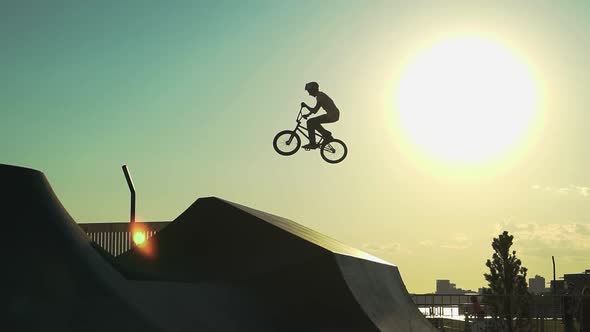 A cyclist on a BMX makes a jump against the background of the sunset