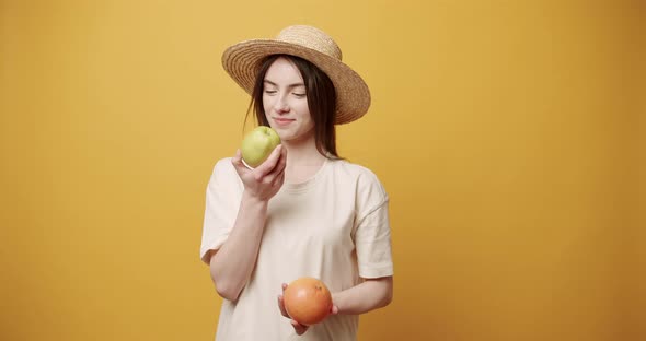 The Beautiful Lady Smells an Apple and an Orange Hugs Them on Yellow Background