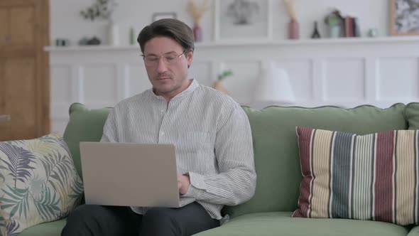 Man Looking at Camera while using Laptop on Sofa