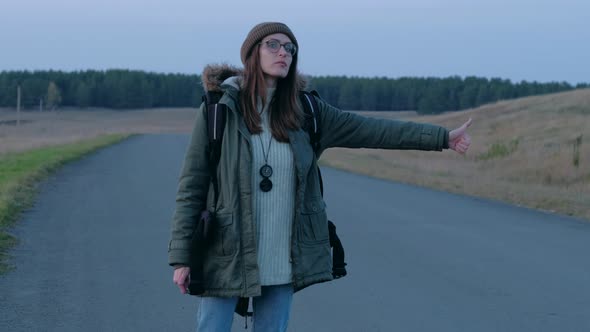 Female Tourist Can't Catch a Car in Evening Walking Along the Road