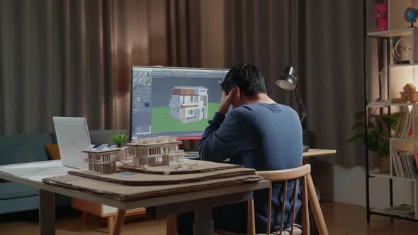 Asian Male Engineer Having A Headache While Designing House On A Desktop At Home