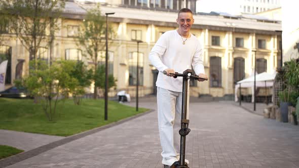 Wide Shot Happy Relaxed Handsome Young Man Riding Escooter to Camera Laughing in Slow Motion