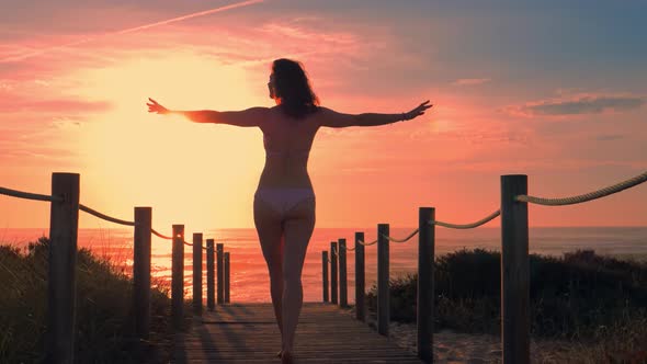 Young Woman Silhouette in a Wooden Foot Bridge at the Beach at Sunset