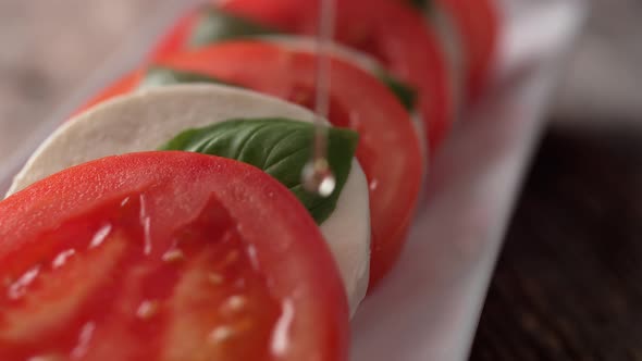 Camera follows pouring olive oil over tomato and mozzarella cheese salad. Slow Motion.