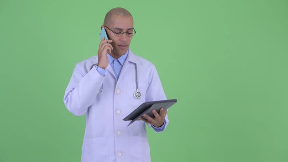 Happy Bald Multi Ethnic Man Doctor Using Digital Tablet and Talking on the Phone