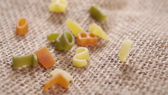 Uncooked multicolored letters of italian alphabet pasta falling on a rustic rough burlap. Macro