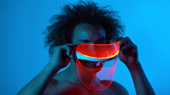 Man wearing light therapy mask against blue wall