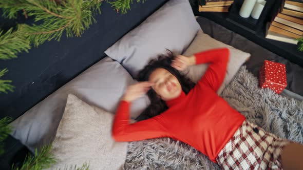 Happy young woman lying in bed. Woman in living room beautifully decorated with xmas tree and lights