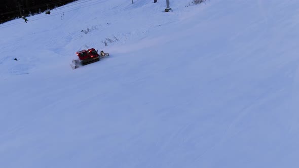 Modern Red Snowcat Drives Up White Track Under Ski Lift