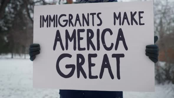 A Person in the Winter Park is Holding a Banner Immigrants Make America Great
